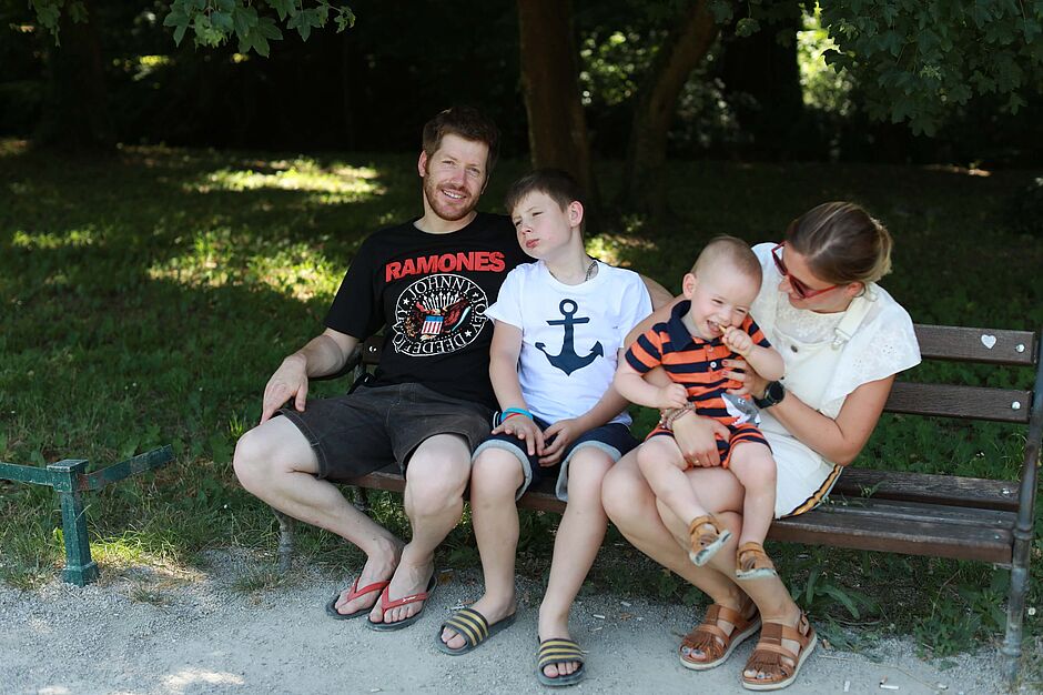 Vesela obitelj koju čine tata, mama i dva sina u parku na klupi. 